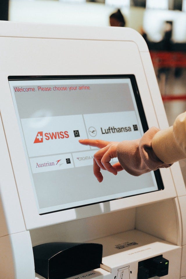 A hand pointing towards one of 5 airlines shown on a screen. It is a touch-screen kiosk for easy airline check-in.