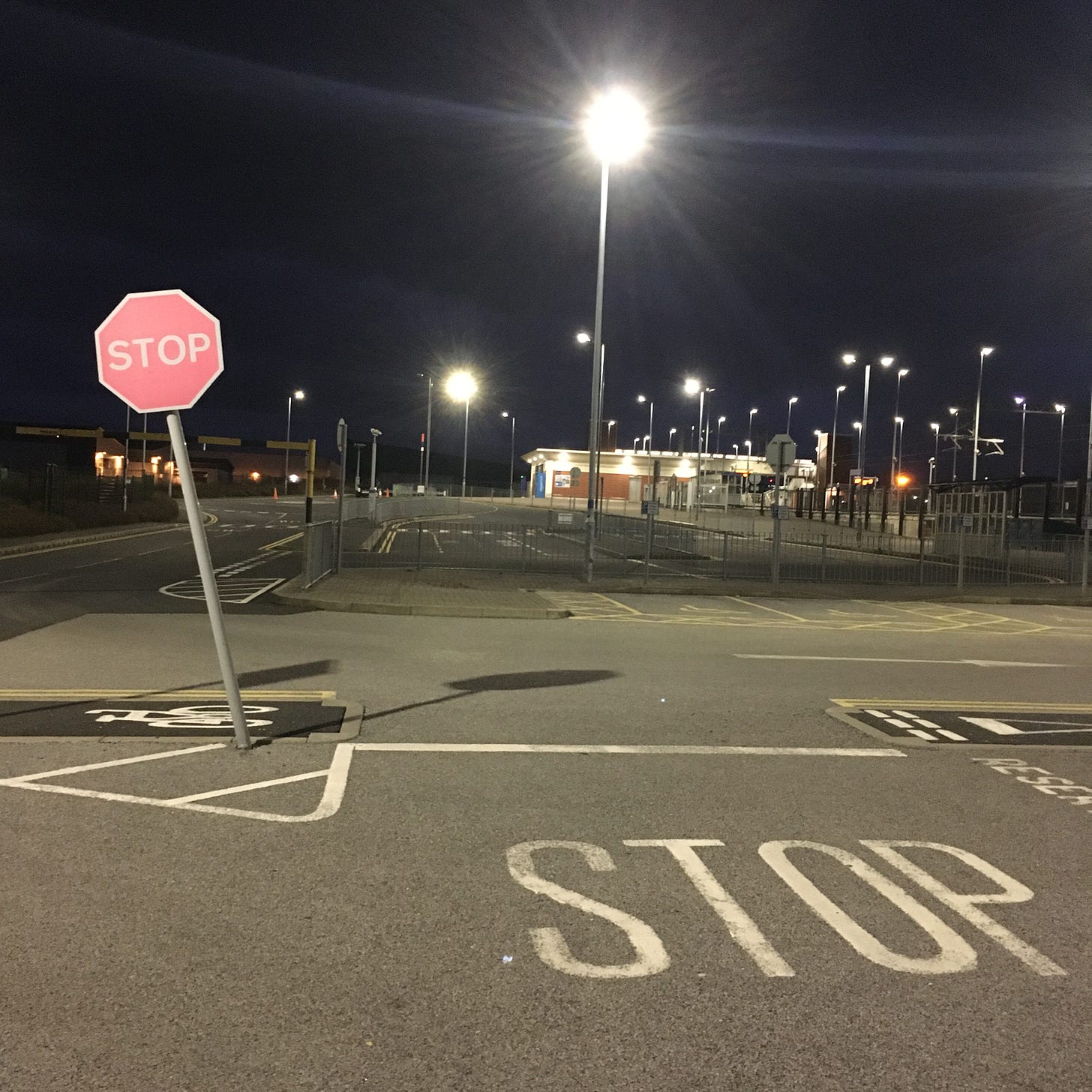 A photo of a carpark at night. There is a red stop sign and STOP is written on the ground