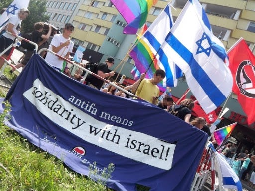 protesting with a banner that reads “antifa means soldiarity with israel” at a rally with Israeli flags and antifa flags