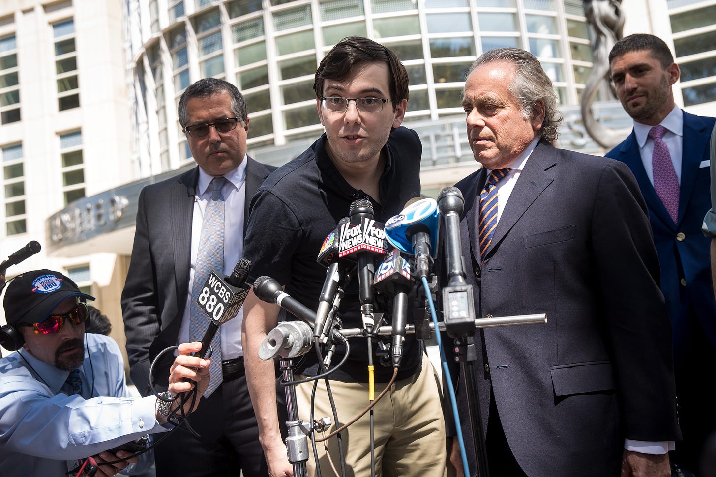 Martin Shkreli speaking to the press after his conviction. He is standing between lawyer Marc Agnifilo (right) and Benjamin Brafman (left). Defense lawyer Jacob Kaplan is standing behind Brafman. (Getty Images.)