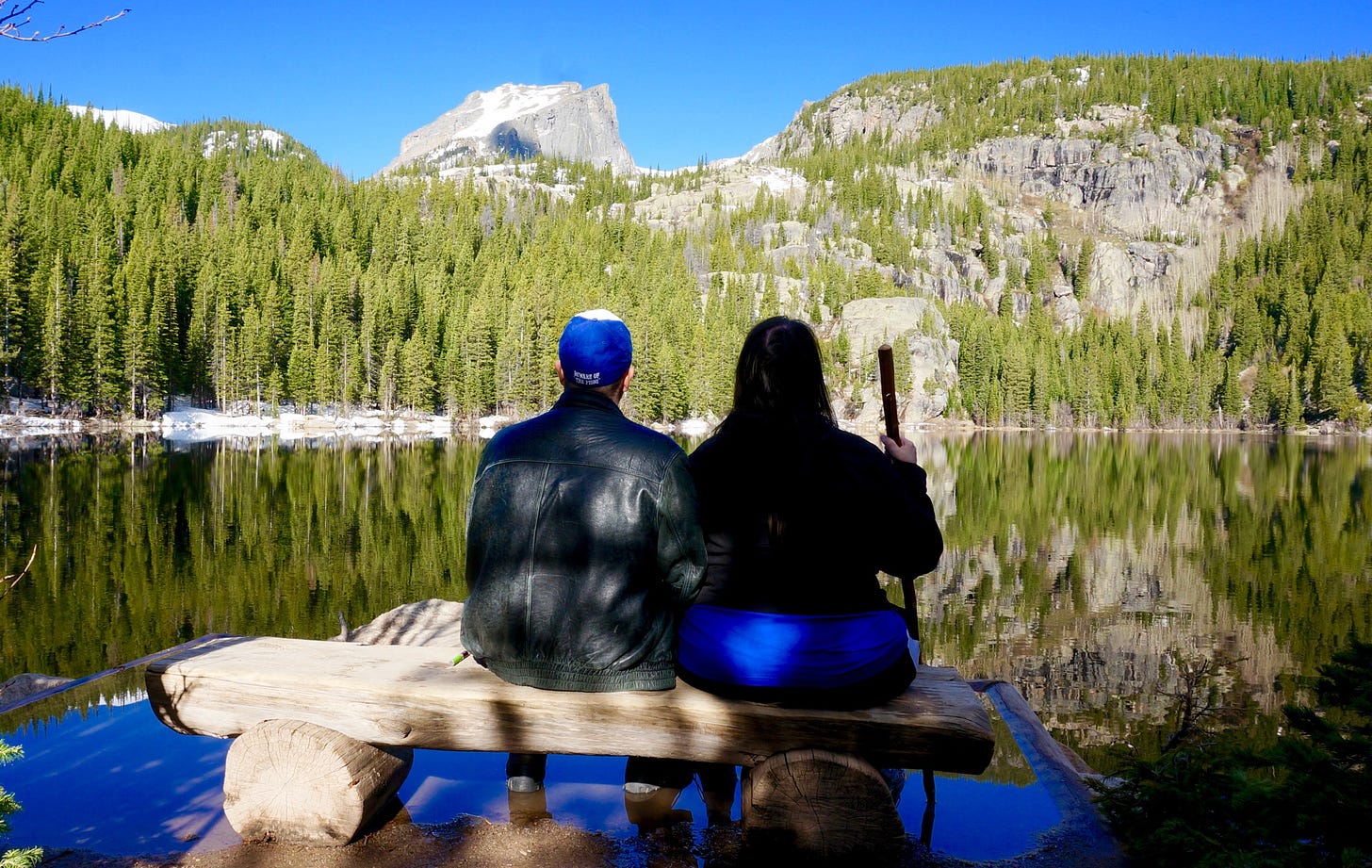 A serene lake scene in Rocky Mountain National Park. The author and her husband are seated in the foreground on a bench