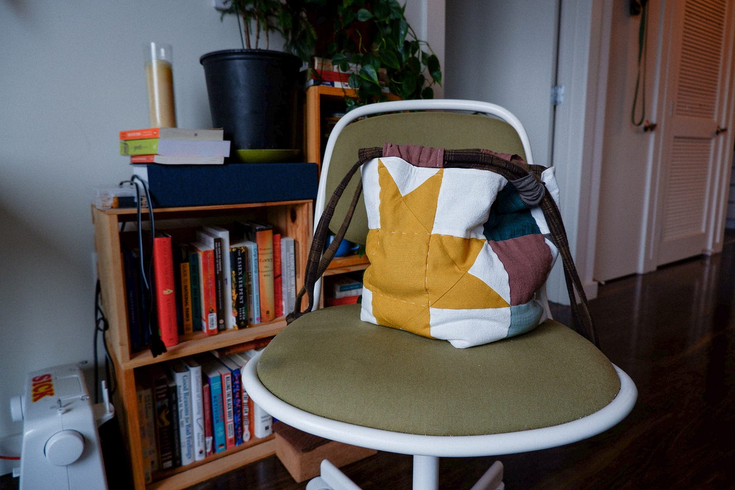 quilted bag with a yellow star sitting on a green and white rolling chair. the chair is in front of crate bookshelves with plants and a printer on top