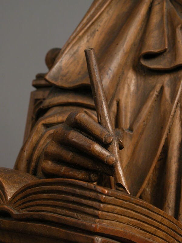 Närbild av träskulptur: en hand med en penna i.