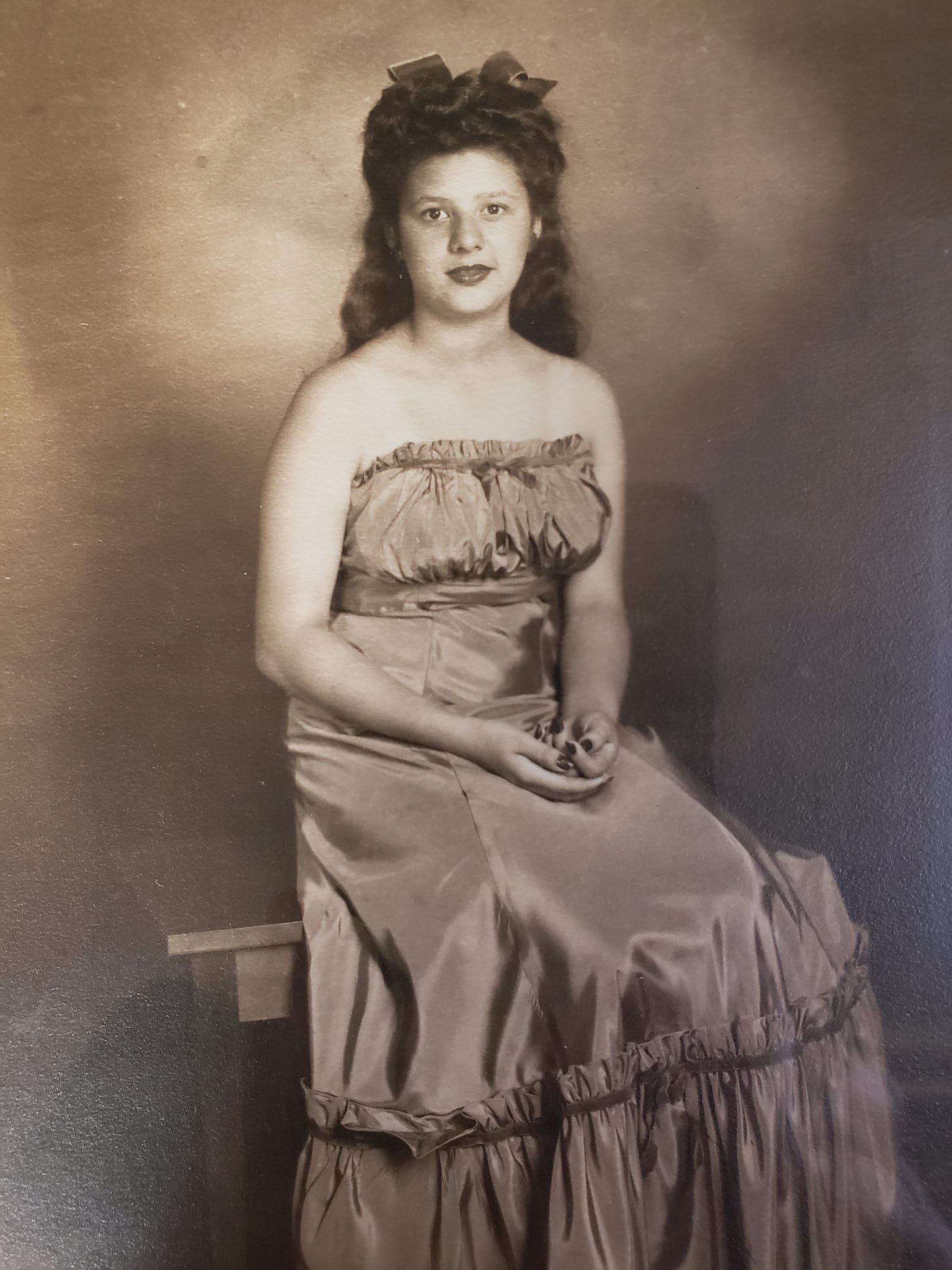 Photograph of Anita Juarez as a young woman, posing in a dress, seated, hands in lap