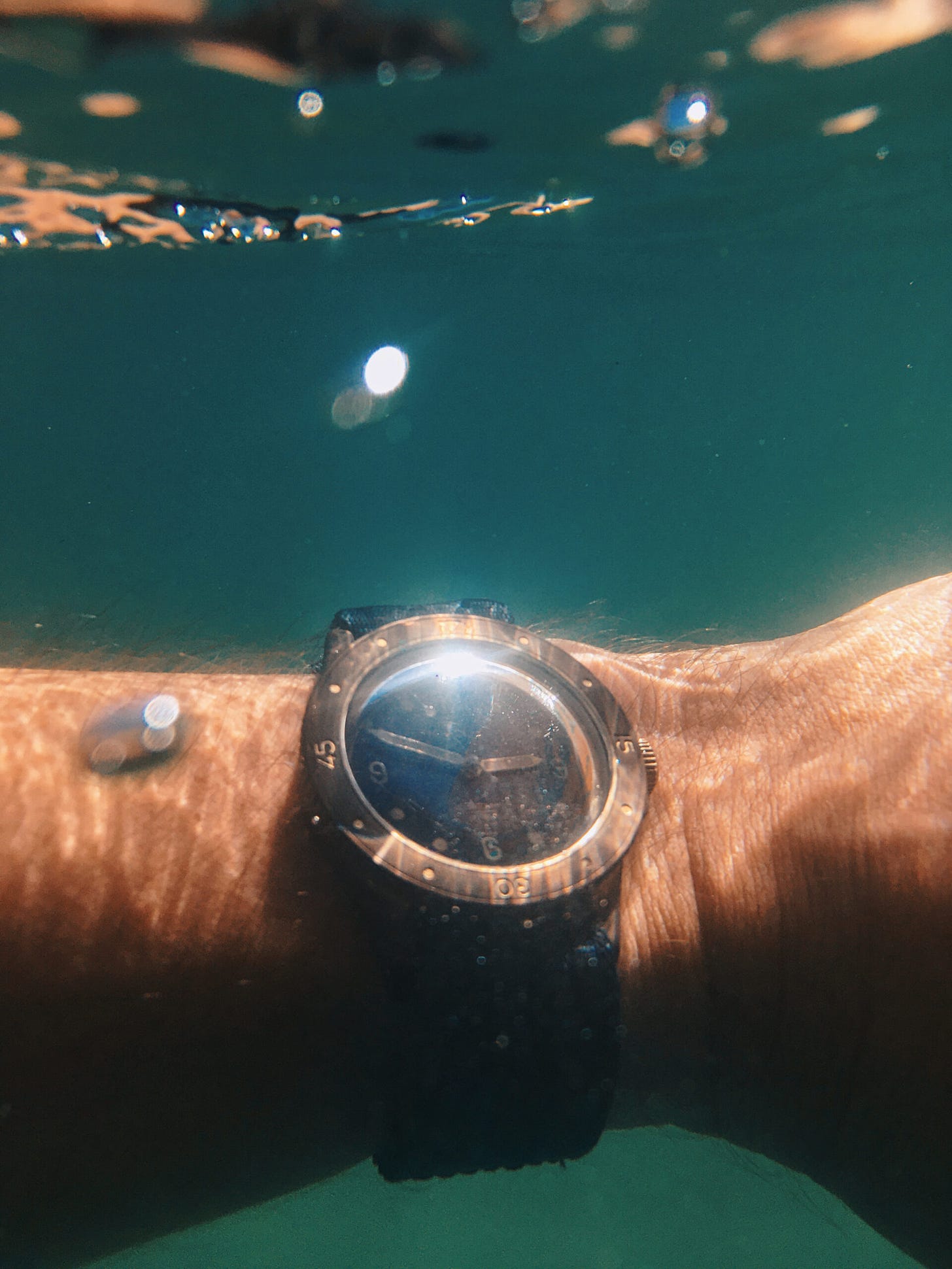 Baltic Aquascaphe Bronze on wrist underwater shot, with two bubbles in foreground and the surface of the water close above