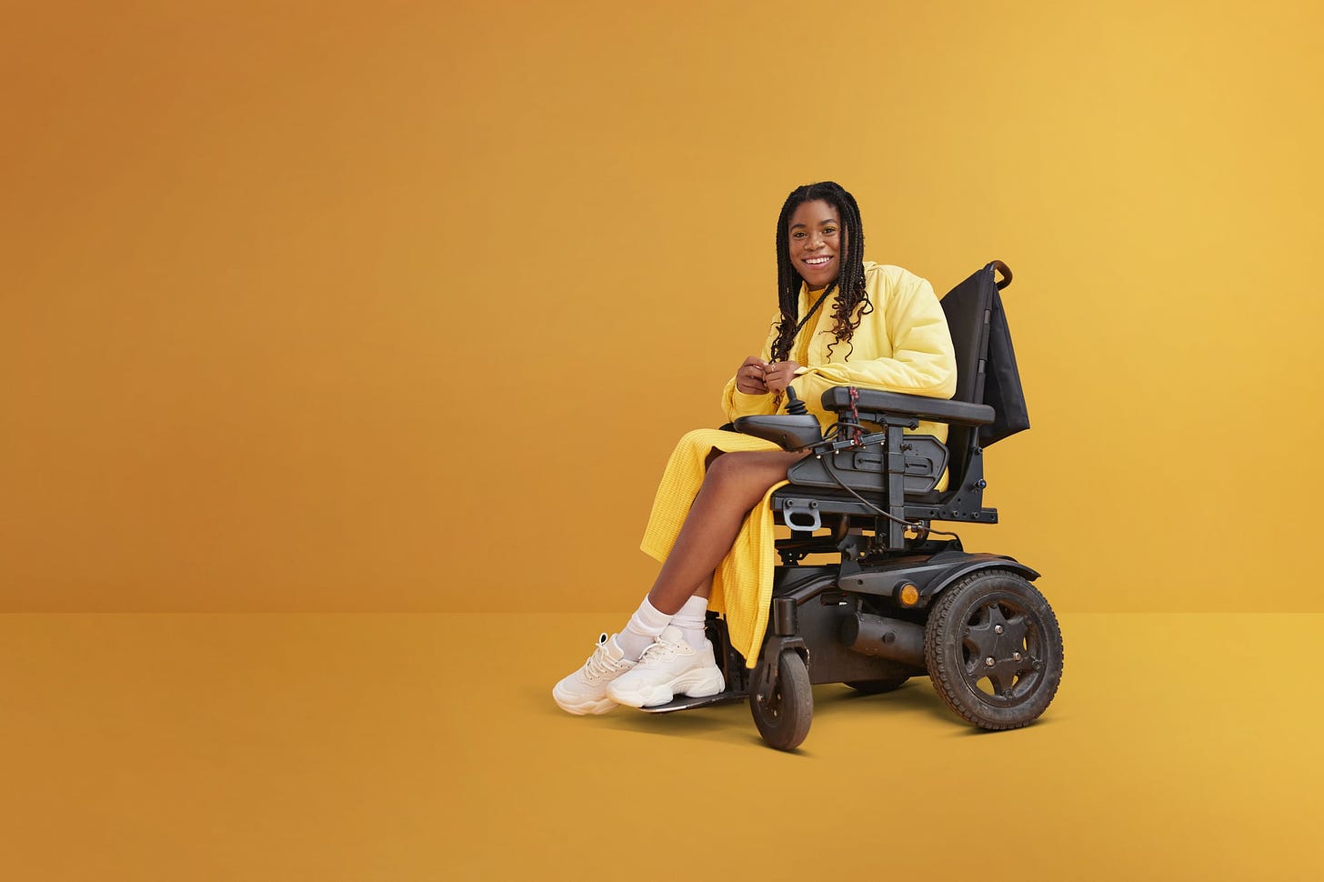 Full length portrait of smiling young woman with disability sitting in wheelchair against yellow background