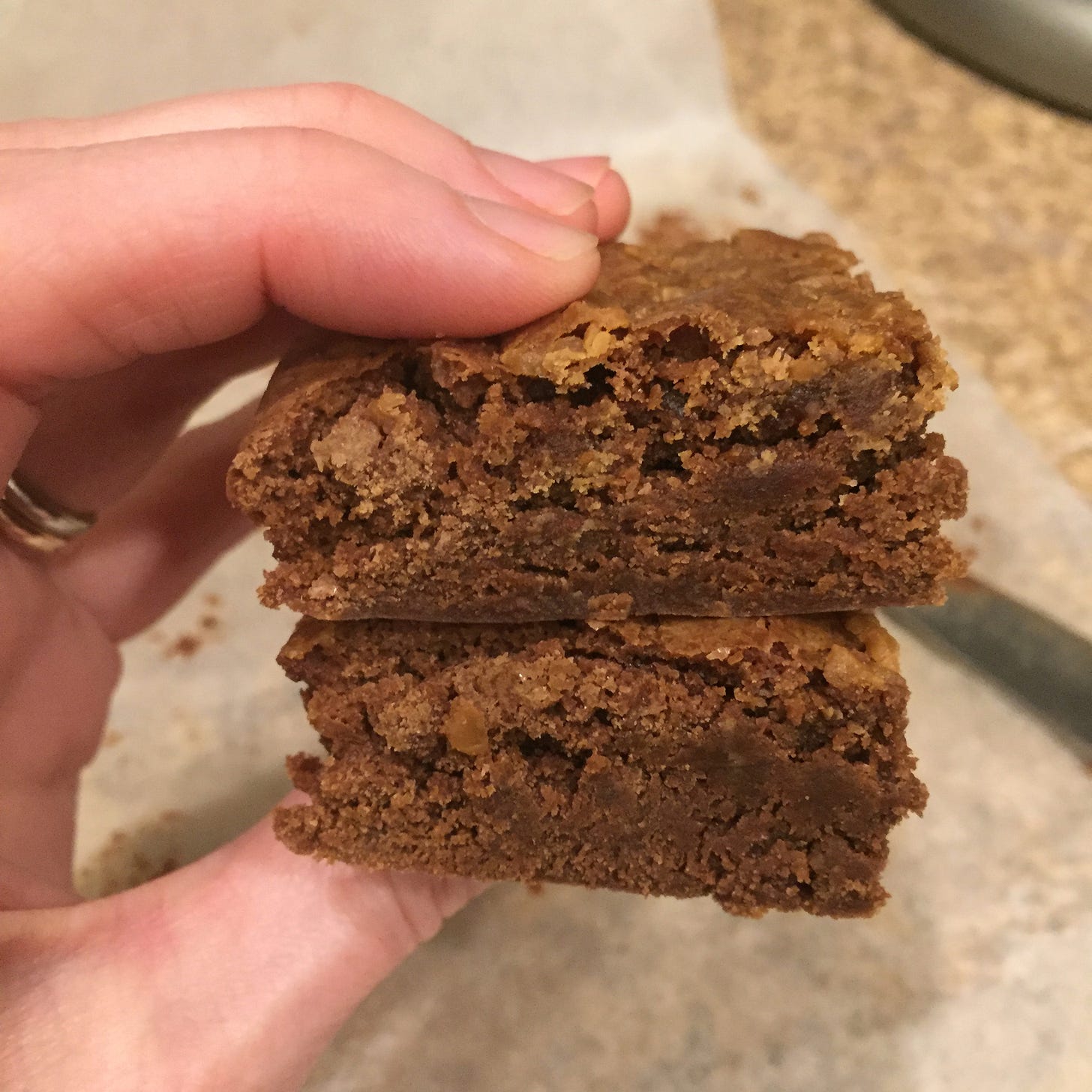 My hand holding two brownies stacked on top of each other. A knife and a piece of parchment paper can be seen in the background.