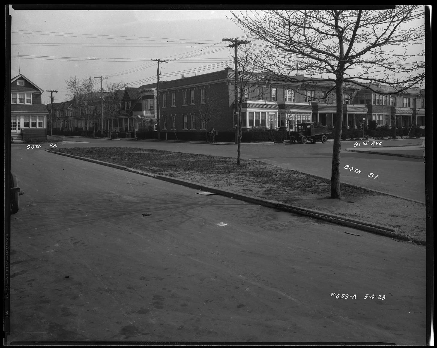 Image shows a photograph from May 1928, before the Whiting Square memorial was created. The median strip in the middle of 84th street is barren but for two trees. 
