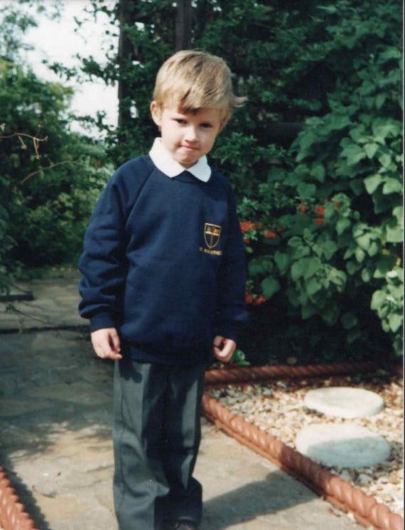 A boy in a British school uniform, standing in a patio garden