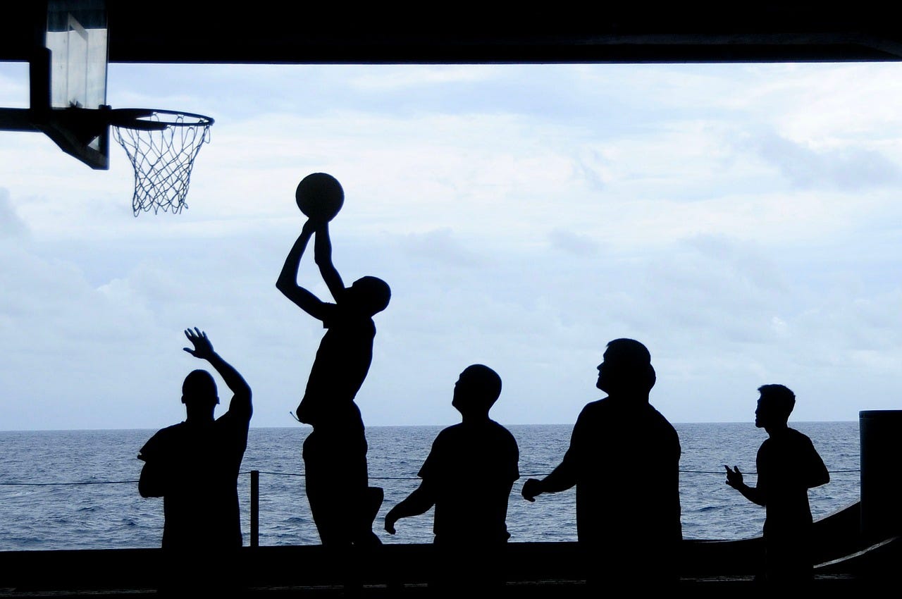 silhouettes of people playing basketball against ocean and sky
