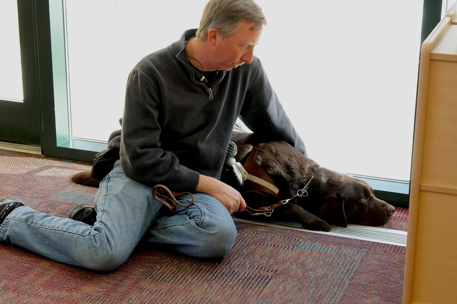 Todd Fahlstrom sits on the floor looking down at his chocolate lab seeing-eye dog