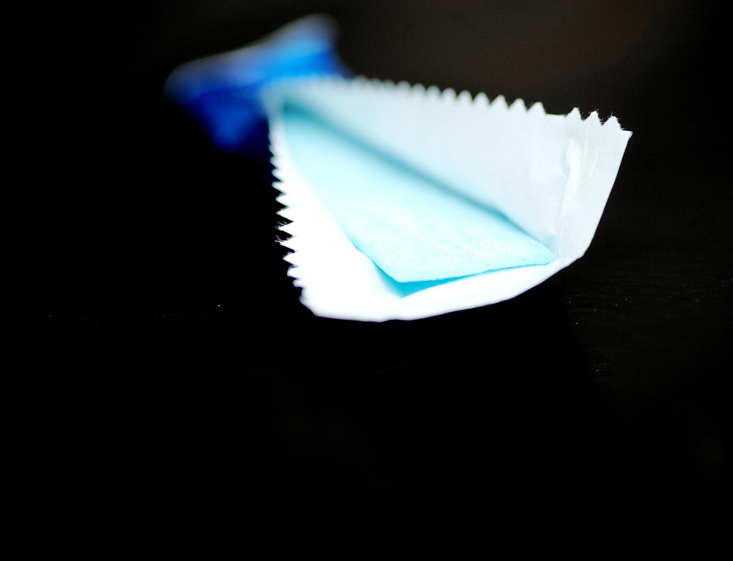 A stick of light blue chewing gum, partially unwrapped