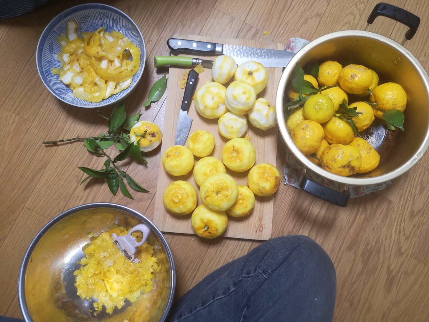 peeled yuzu fruit on a cutting board on the floor, fruit and peels in bowls