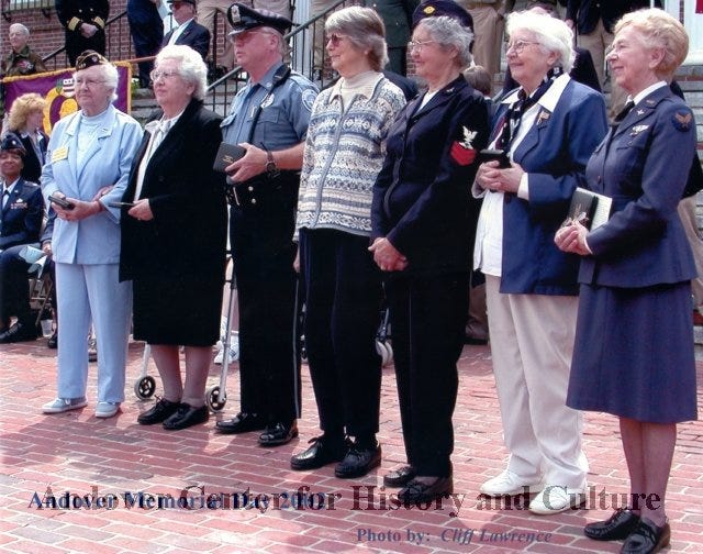six elderly white women and one white man stand on brick sidewalk 