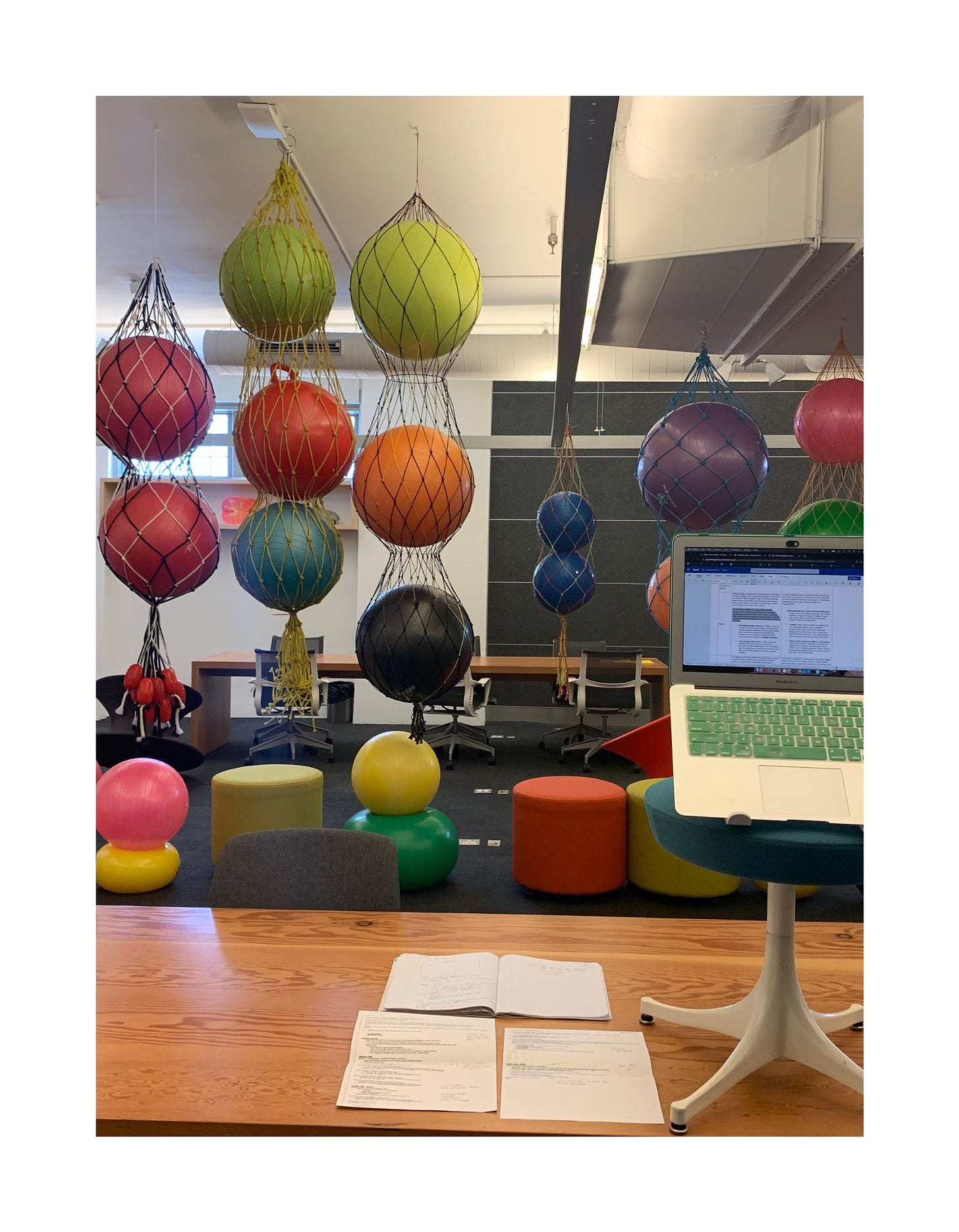 An office with installation art featuring several nets filled with colorful medicine balls.