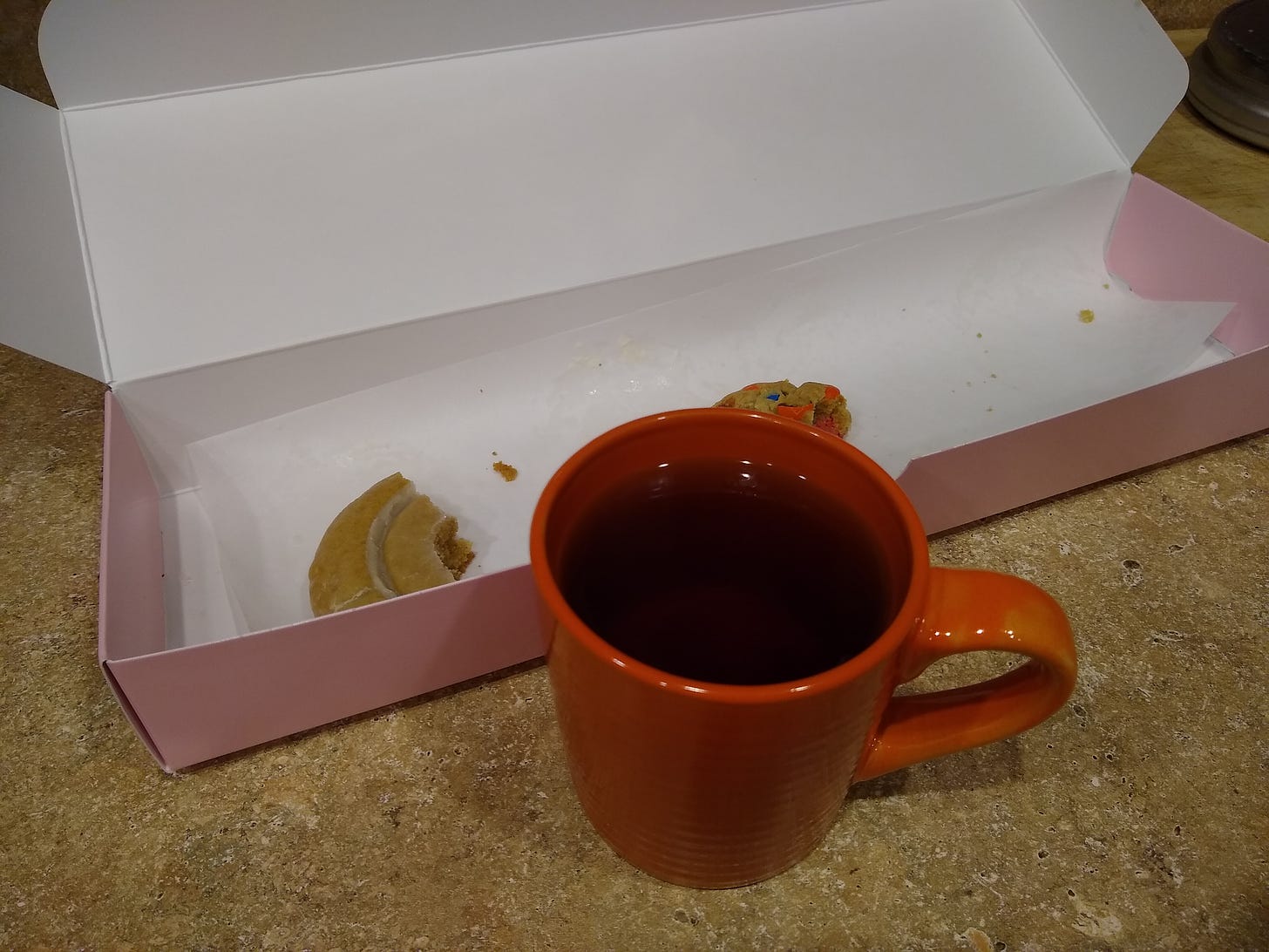 Mug of apple cider and a mostly empty box of Crumbl cookies.