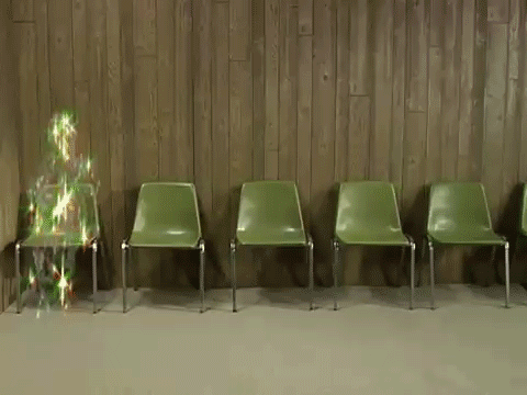a line of 5 olive green chairs face us, set against a wooden wall behind them. on the first chair to our left, is a shimmering glittery shape flickering, it's a sort of human form but who knows what it is. let's call it 'essence'