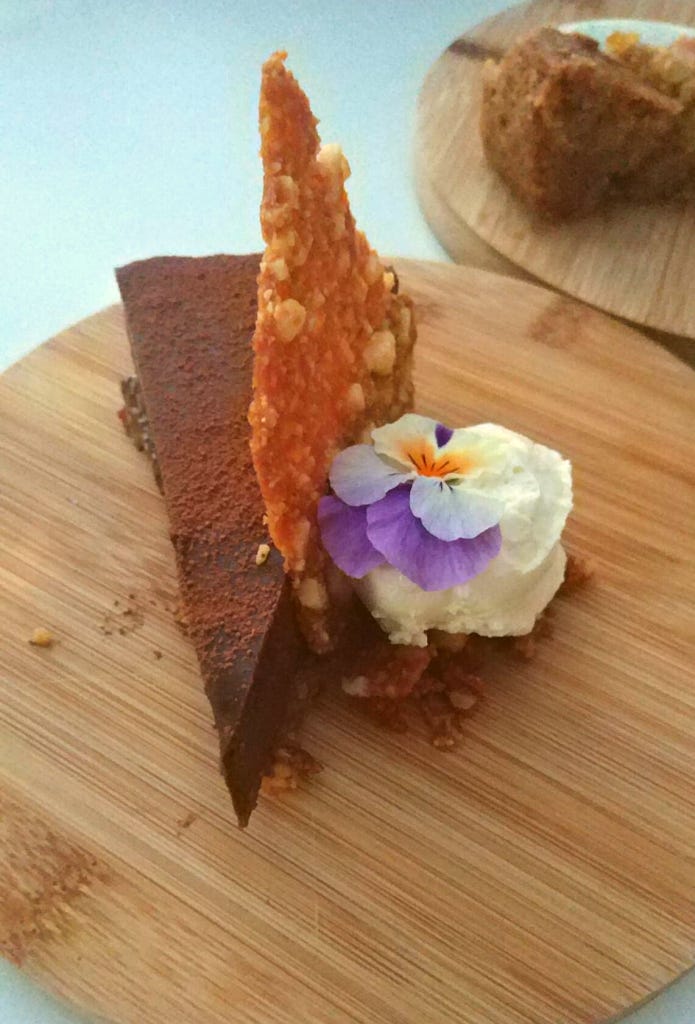 A slice of chocolate torte, served with a purple pansy, honey whipped cream and praline