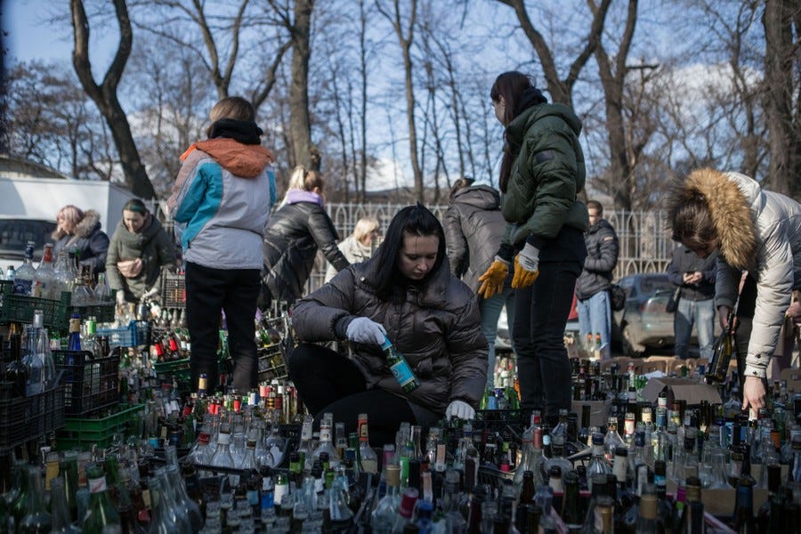 People gather among hundreds of empty bottles in a park, preparing them to be used as Molotov cocktails.