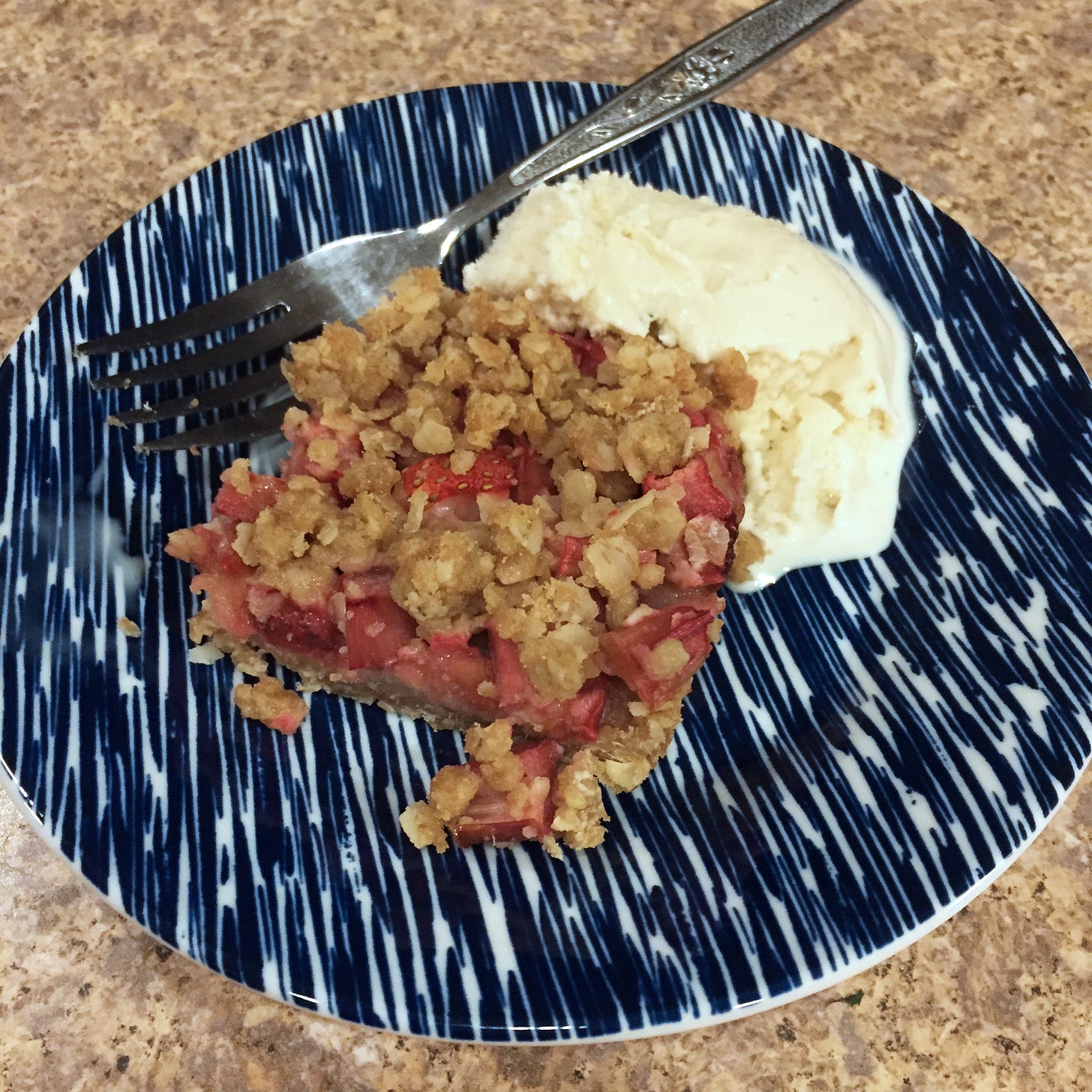 a square of strawberry rhubarb crisp, crumbling at the edges, next to a scoop of ice cream, on a blue striped plate.
