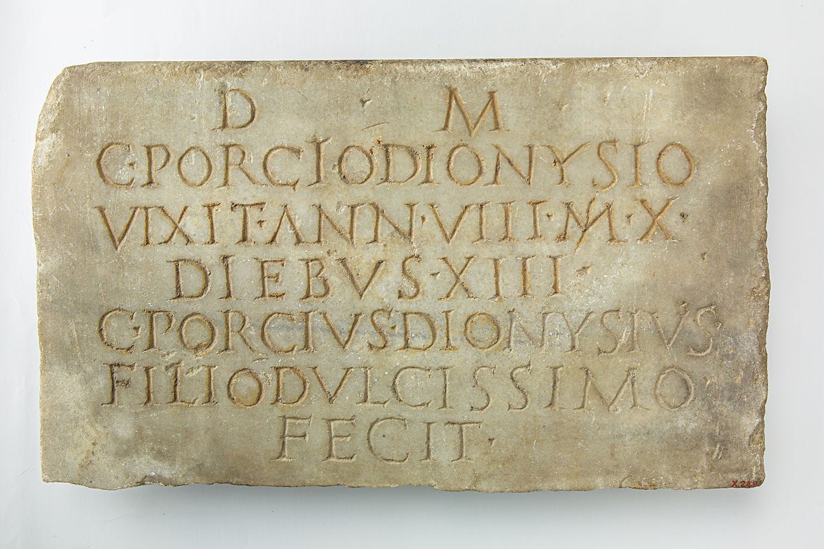 Inscrição em mármore gravado provavelmente entre os séc. I e II, no acerto do The Metropolitan Museum of Art. Embora o Y não estivesse no alfabeto romano comum, era usado para nomes de origem grega, como a referência a Pórcio Dionísio.