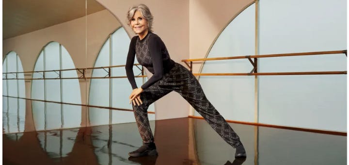 Jane Fonda, in a lunge pose in an exercise studio, smiling at the camera