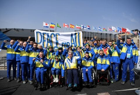 Ukraine Chef De Mission Valerii Sushkevych and members of team Ukraine hold a banner up reading 'Peace for All' in the Athletes Village on March 10.