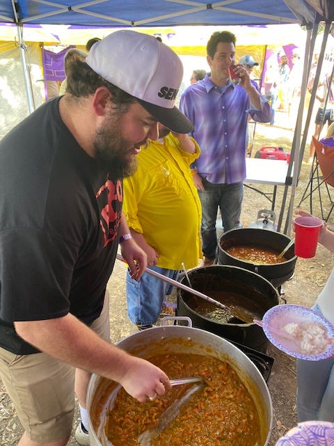 Three men stand behind three large pots of food, ready to serve eager eaters just out of frame. Jay, a man who looks every bit the former D1 football player he is, serves etouffee in the foreground.