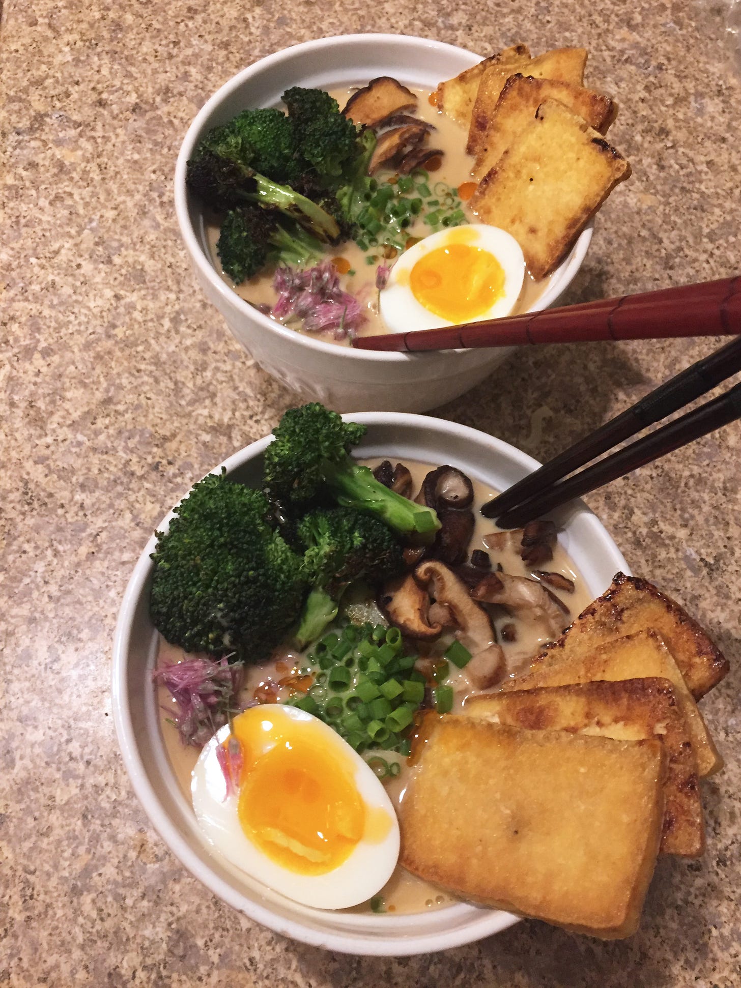 two white bowls of ramen with chopsticks in each, covered with a neat arrangement of the ingredients listed below.