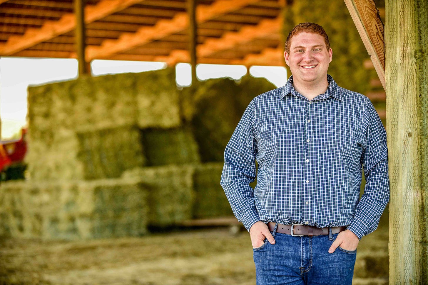 man in checkered shirt and jeans with hands in pockets in barn