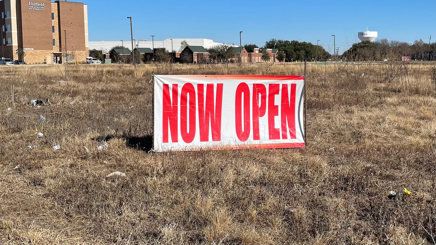 A "Now Open" sign in an otherwise empty field