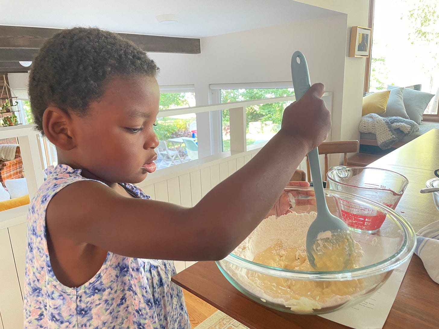 a black kid in a long floral nightgown stirs dough