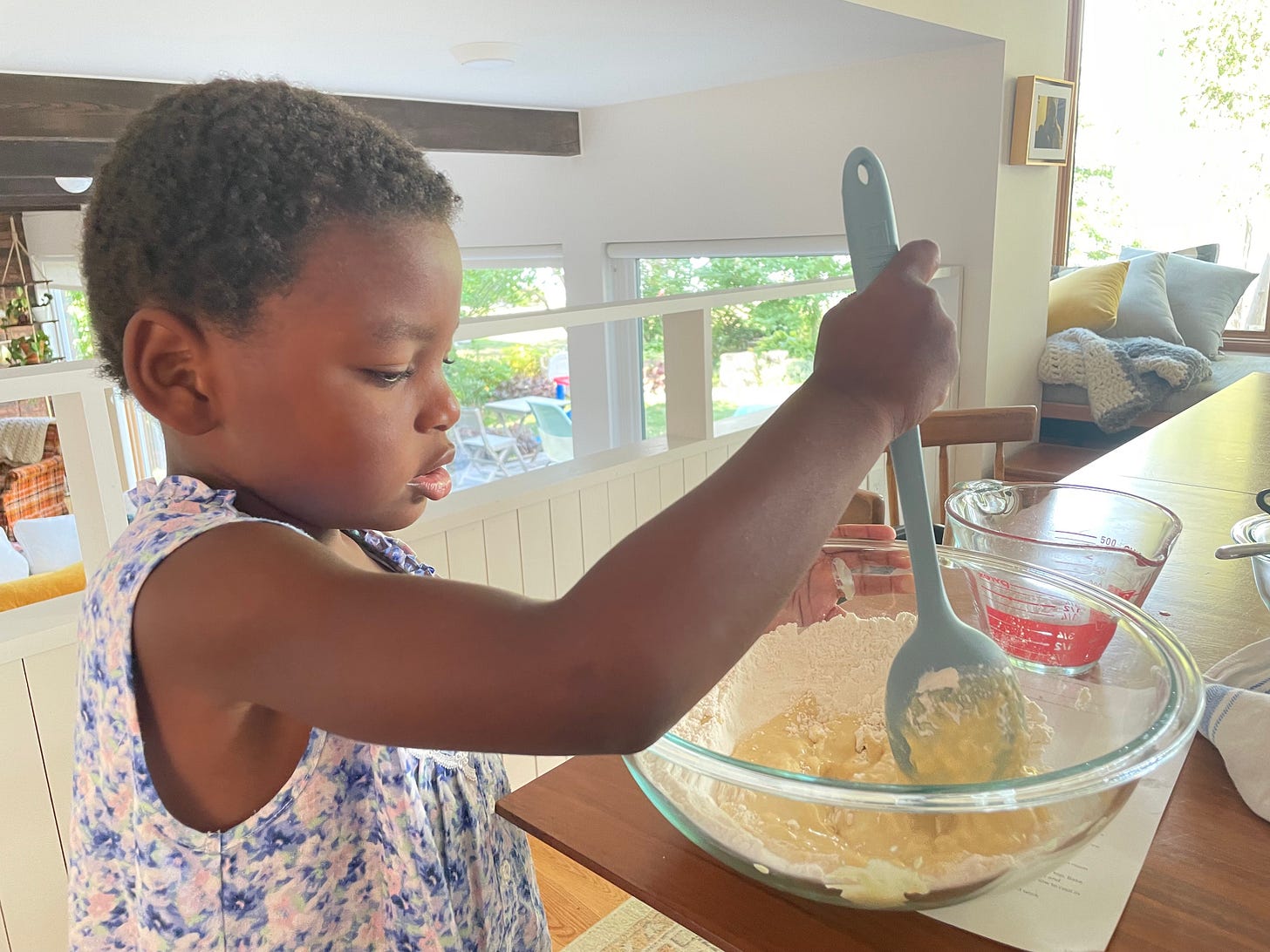 a black kid in a long floral nightgown stirs dough