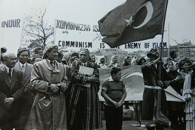 Alptekin, holding a book, leads a demonstration in support of East Turkestan separatism in 1966. Alptekin stands in front of a banner that reads, "Communism is the enemy of Islam."