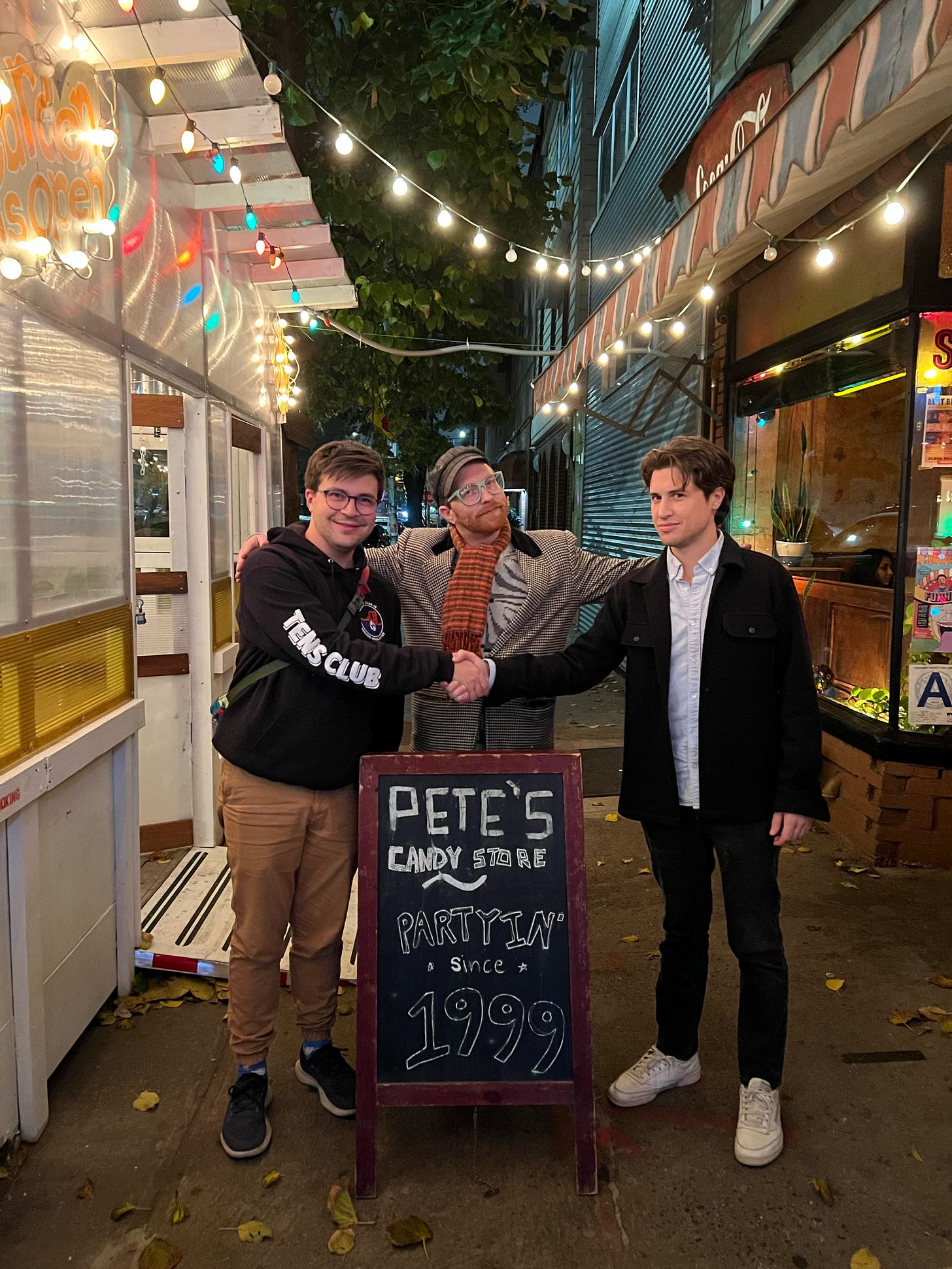 Three white men, all approximately 5'10", stand outside Pete's Candy Store in Greenpoint. The two men on the outer edges shake hands while the third man stands between them with his hands on their shoulders. Three white men, all approximately 5'10", stand outside Pete's Candy Store in Greenpoint. The two men on the outer edges shake hands while the third man stands between them with his hands on their shoulders.