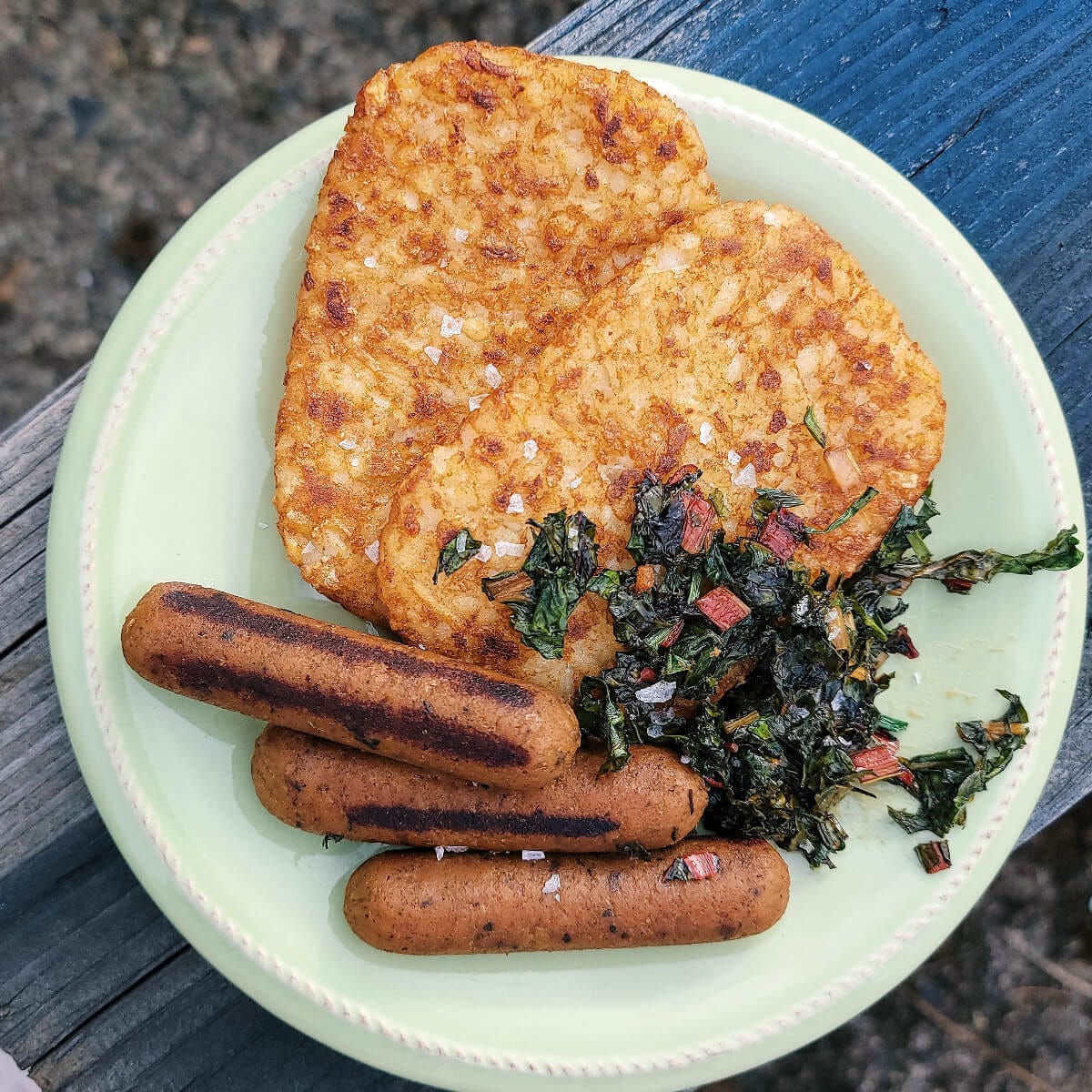 two crispy, golden hashbrowns patties cozied up beneath three, charred veggie sausage links and a small wilted collection of rainbow chard. sprinkled over top of everything is that darn flaky sea salt.