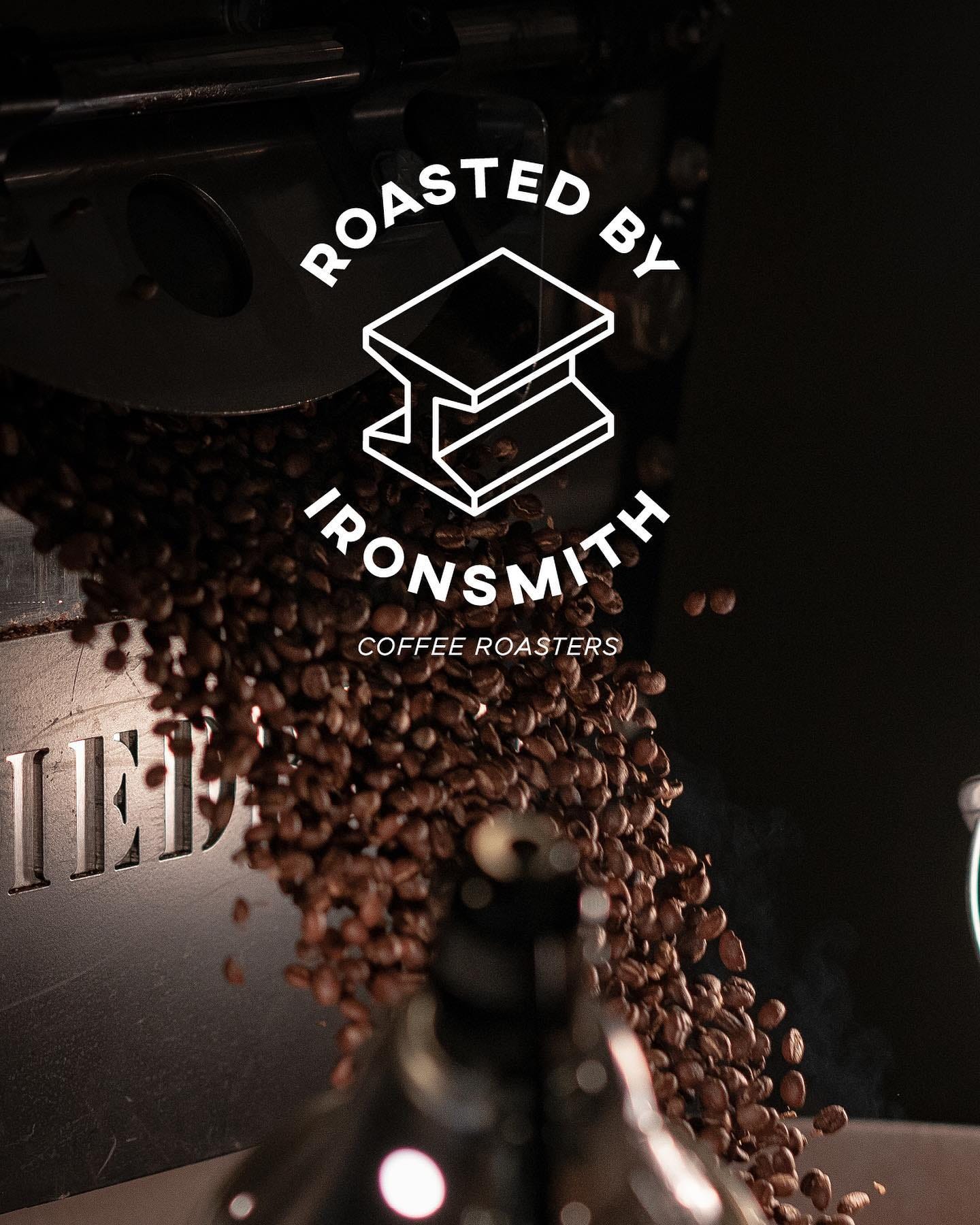 The Ironsmith Coffee Logo imposed over coffee beans in a coffee bean roasting machine.
