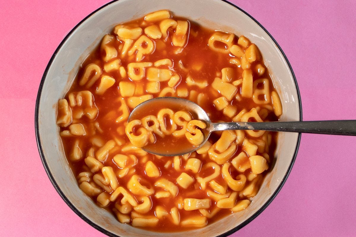 The word “gross” floats on a spoon in a bowl of alphabet Spaghetti-Os on a hot pink background.