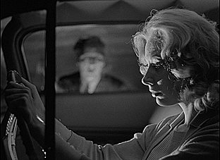 A gif of Mary Henry driving. She looks out the passenger seat window and sees "The Man" -- a ghostly, pale figure -- gawking at her. She jumps, startled.