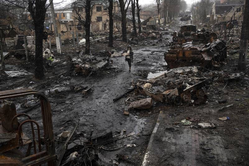 A woman walks alone by destroyed tanks and other debris on a muddy path