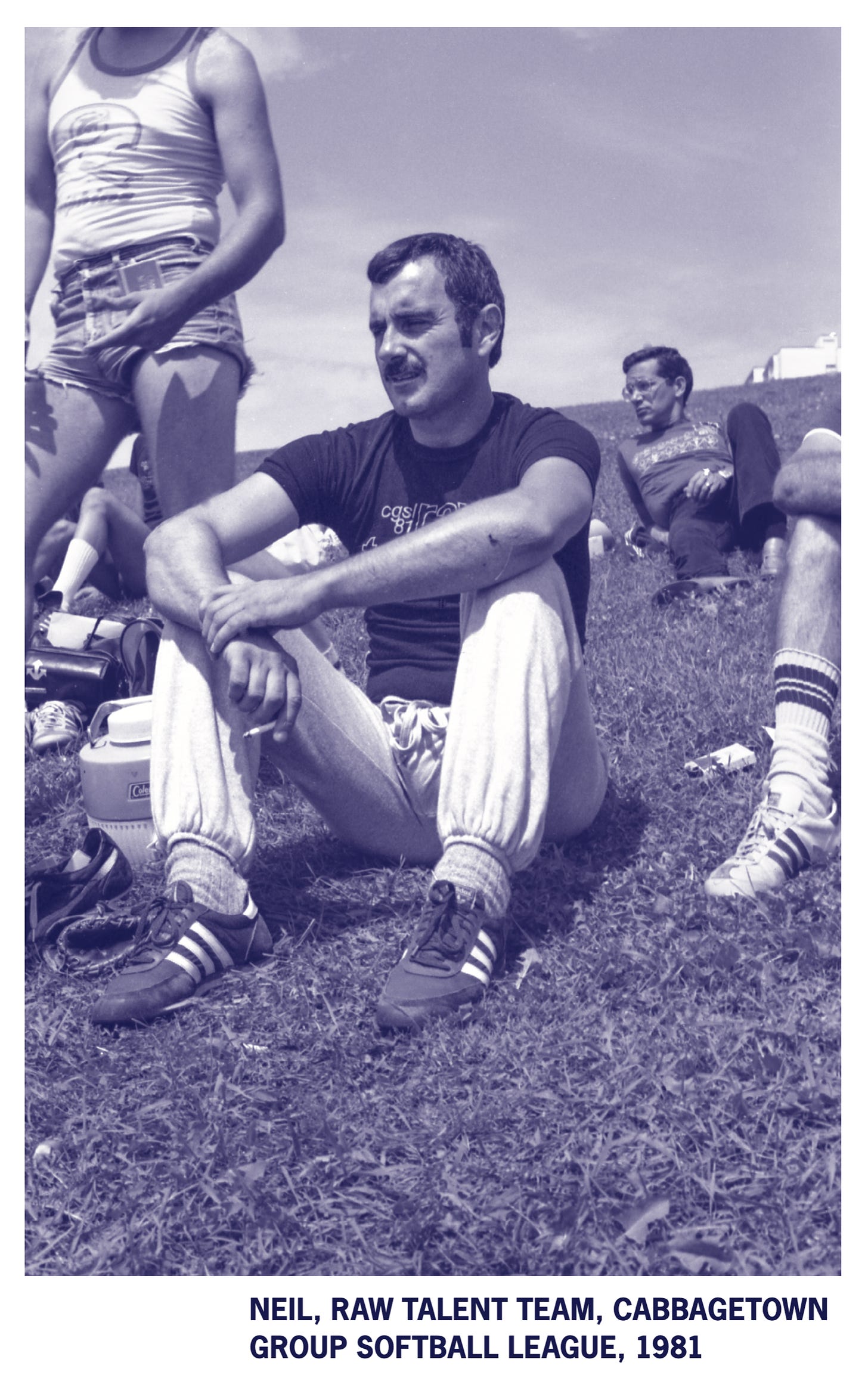 On grass field, players from the Cabbagetown Group Softball League sit watching a game. 1981