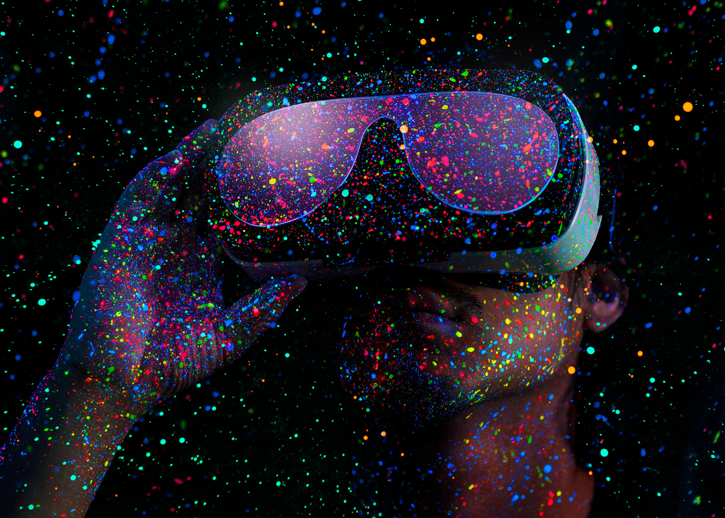 Someone wearing a Virtual Reality headset in a stylized space-field of dayglo splotches. Almost looks like floating paint flecks