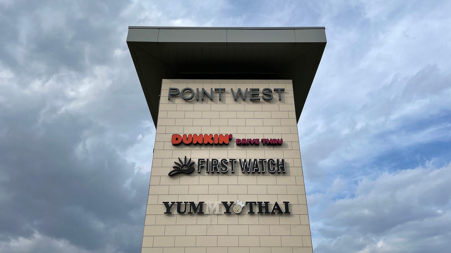 A white brick tower at the Point West development that lists three tenants: Dunkin', First Watch, and Yummy Thai