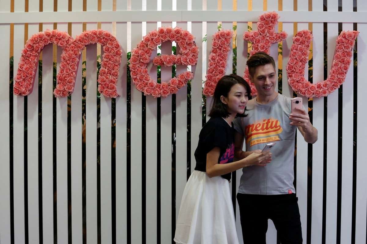 a man standing in front of a fence: Models pose for a photo during Meitu’s IPO news conference in Hong Kong on December 2, 2016. Photo: Reuters