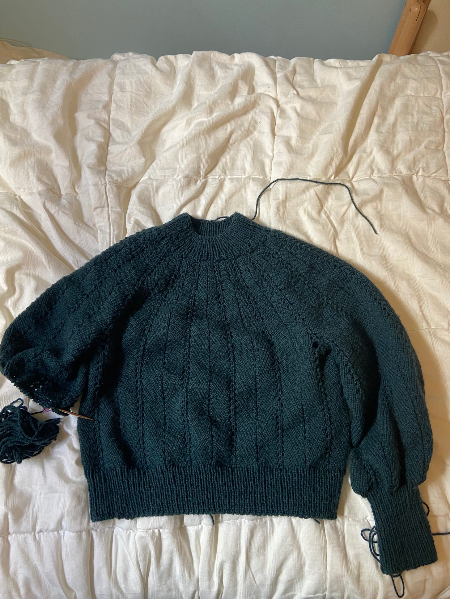 a green sweater with one sleeve half-finished. it has a lacey v-pattern.