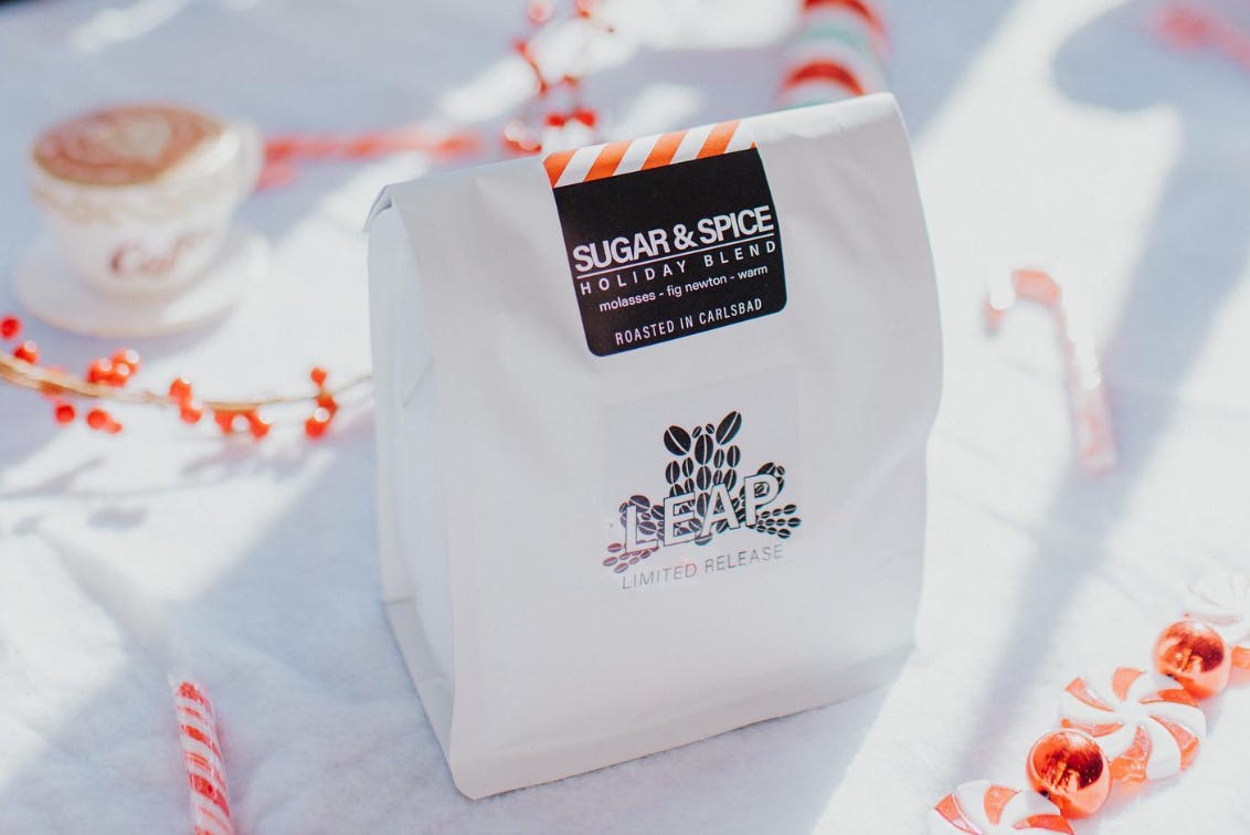 A white bag of Sugar and Spice holiday blend Leap Coffee beans on a table with candy canes strewn about around it.