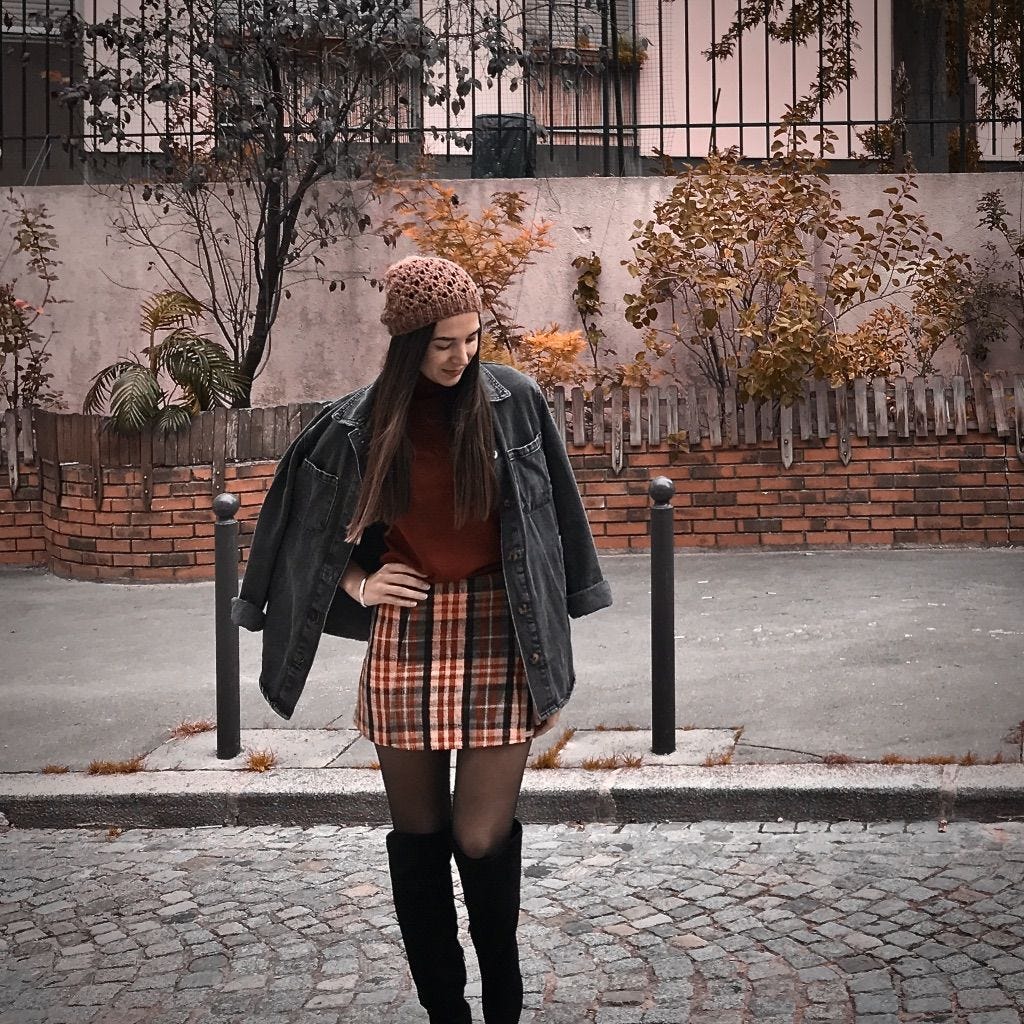 Girl in a street wearing a check skirt, red shirt and a grey jacket over her shoulders