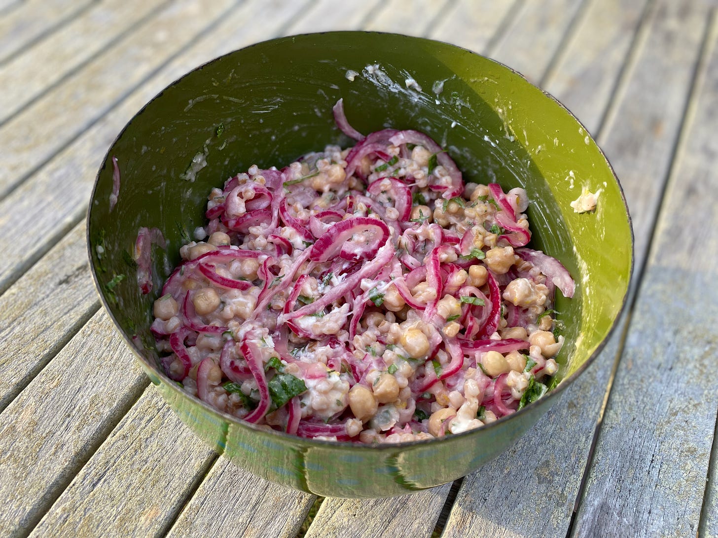 A green bowl of farro salad topped with lots of pickled red onions.