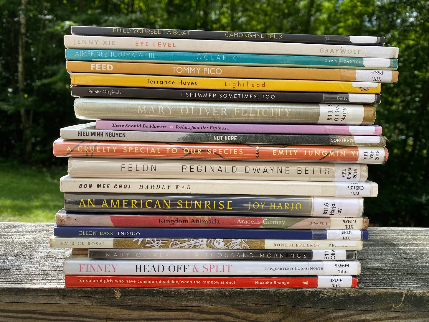 A large stack of poetry books from the library, sitting on a porch railing. They include: for colored girls who have considered suicide/when the rainbow is enuf, Head Off & Spit, A Thousand Mornings, Boneshepards, Indigo, Kingdom Animalia, An American Sunrise, Hardly War, Felon, A Cruelty Special to Our Species, Not Here, There Should be Flowers, Felicity, I Shimmer Sometimes, Too, Lighthead, Feed, Oceanic, Eye Level, and Build Yourself a Boat.