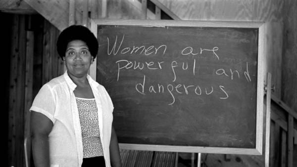 Audre Lorde  standing beside a chalkboard that reads "Women are powerful and dangerous".